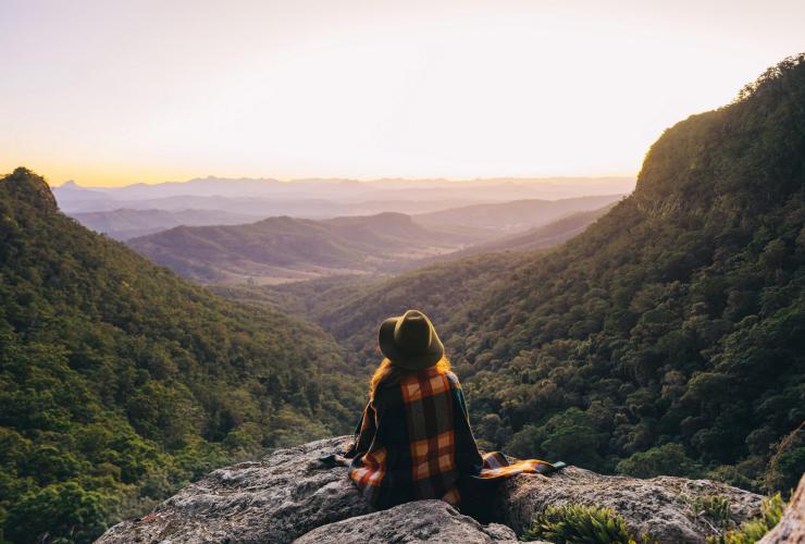 A person sitting at the top of a peak in Lamington National Park overlooking rolling mountains covered in trees in Queensland © Tourism and Events Queensland