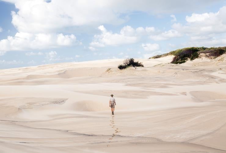 A person walking up a stretch of white sand dunes, leaving footprints behind them at Tookee Sand Blow, K’gari (Fraser Island) Great Walk, K’gari, Queensland © Tourism and Events Queensland