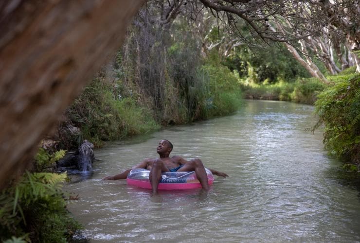 A man floating down the clear stream of Eli Creek on an inflatable device while looking up at the trees surrounding him on K’gari, Queensland © Tourism and Events Queensland