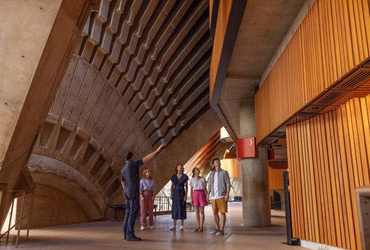 A group of people standing with a tour guide as he shares insights into the complex structure of the Sydney Opera House, Sydney, New South Wales © Tourism Australia