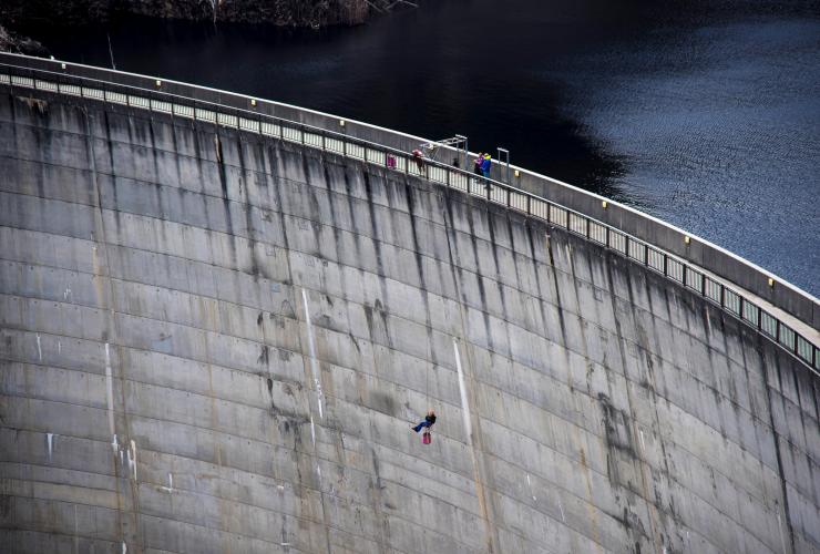 Aerial view of a person abseiling down Gordon Dam with three people standing on the platform above in Strathgordon, Tasmania © Rob Burnett