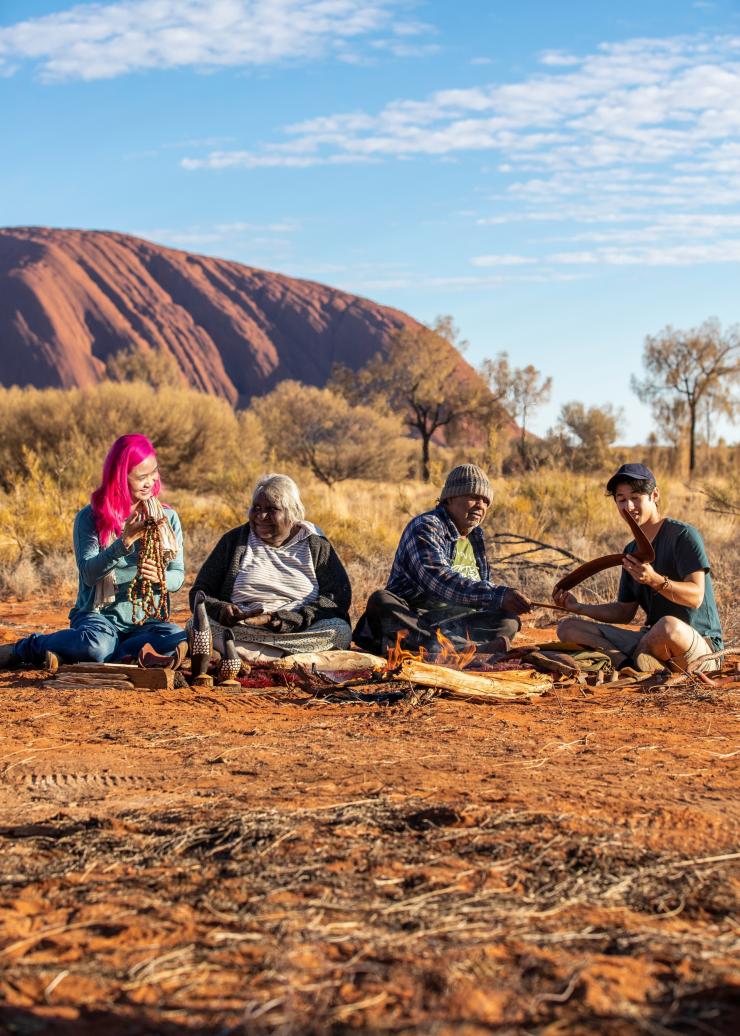 A couple seated with two local Aboriginal artists in front of Uluru during a tour with Maruku Arts, Uluru-Kata Tjuta National Park, Northern Territory © Tourism NT/Helen Orr