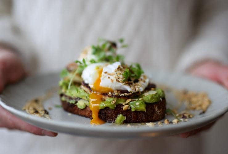 A person holding a plate with avocado on toast topped with runny poached eggs at The Depot, Bondi, New South Wales © The Depot
