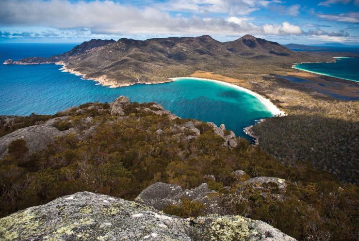 Aerial view over a green, mountainous peninsula with a curved white sand beach and bright turquoise water at Wineglass Bay, Freycinet National Park, Tasmania © Tourism Tasmania