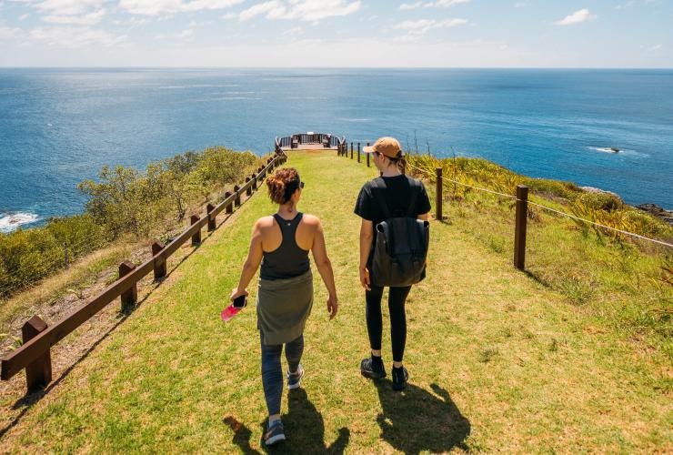 Two people walking along a grassy headland overlooking the ocean at Captain Cook’s Lookout, Norfolk Island © Tourism Australia