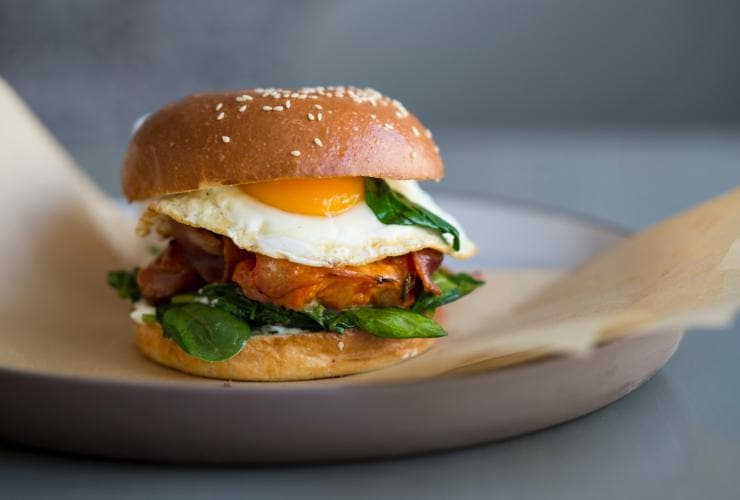 A bacon and egg roll with greens on a plate at Kepos Street Kitchen, Sydney, New South Wales © Kepos Street Kitchen