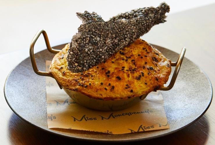 A meat pie in a small pan with two handles topped with a decorative squid ink cracker at Miss Moneypenny's Broadbeach, Gold Coast, Queensland © Tuscany Gray/ Miss Moneypenny's