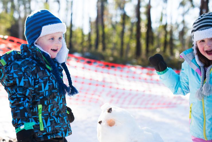 Children standing beside a snowman while laughing at Corin Forest Mountain Resort, Australian Capital Territory © VisitCanberra