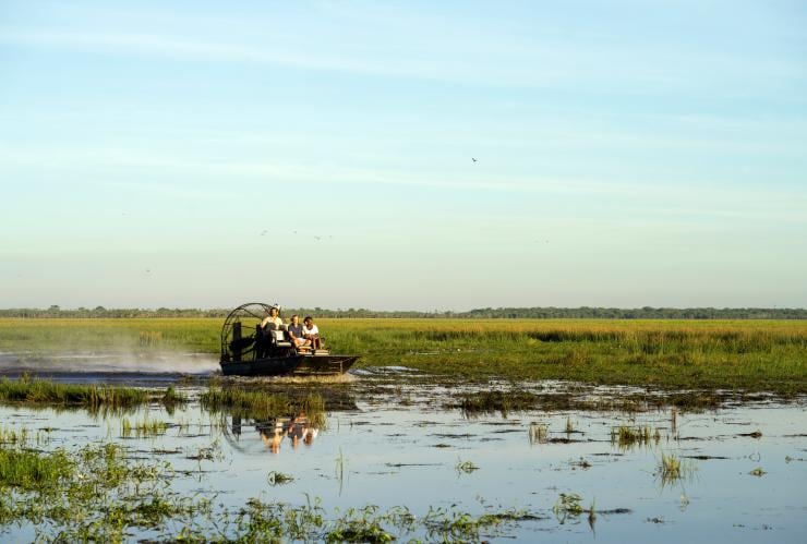 Two people riding with a tour guide on an airboat across wetlands on a sunny day at Bamurru Plains, Kakadu National Park, Northern Territory © Tourism NT