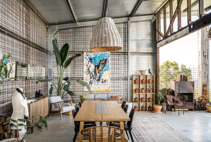 A large, open room with a dining table, artworks and pot plants and an open wall letting in sunlight at Blackbird, Bryon Bay, New South Wales © Blackbird/Saul Goodwin @propertyshotphotography
