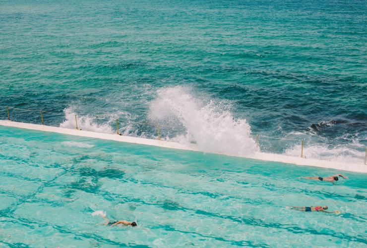 People swimming laps in the clear blue water of Bondi Icebergs Pool as the ocean’s waves crash against the side in Bondi, New South Wales © Tourism Australia