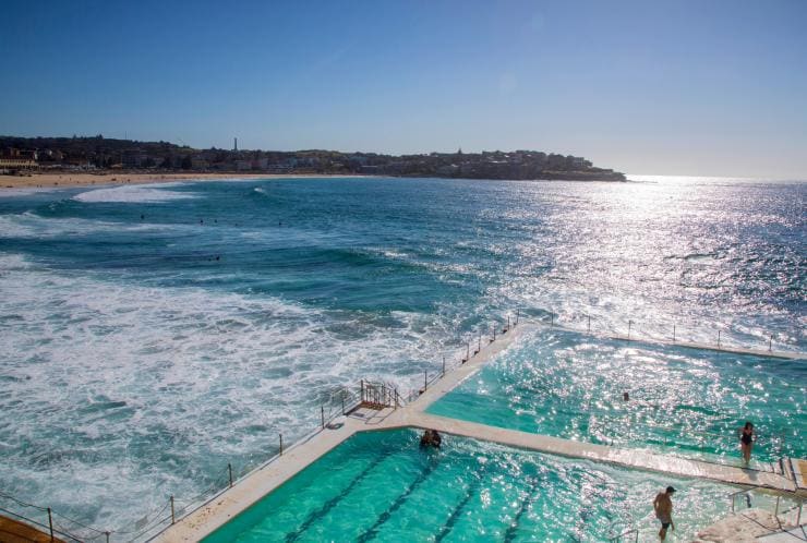 People swimming at Bondi Icebergs in the foreground with surfers and beach-goers in the background on Bondi Beach, Sydney, New South Wales © Destination NSW