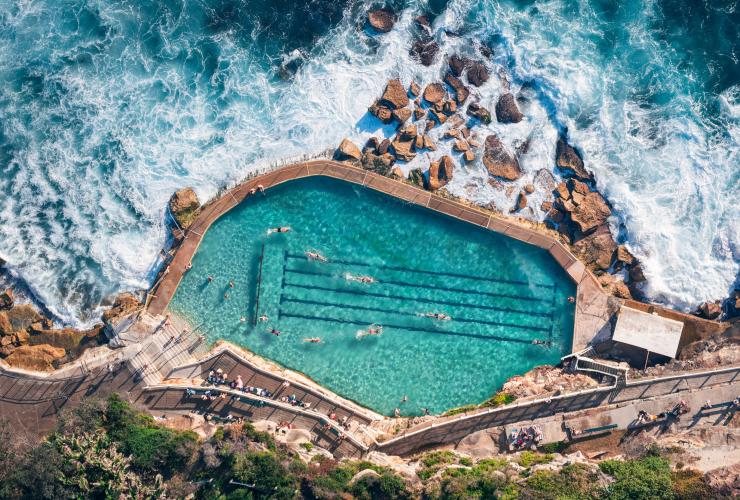 Aerial view over people swimming in the turquoise water of Bronte Baths with ocean waves swirling against the rocks surrounding the pool, Bronte Beach, Sydney, New South Wales © Tourism Australia