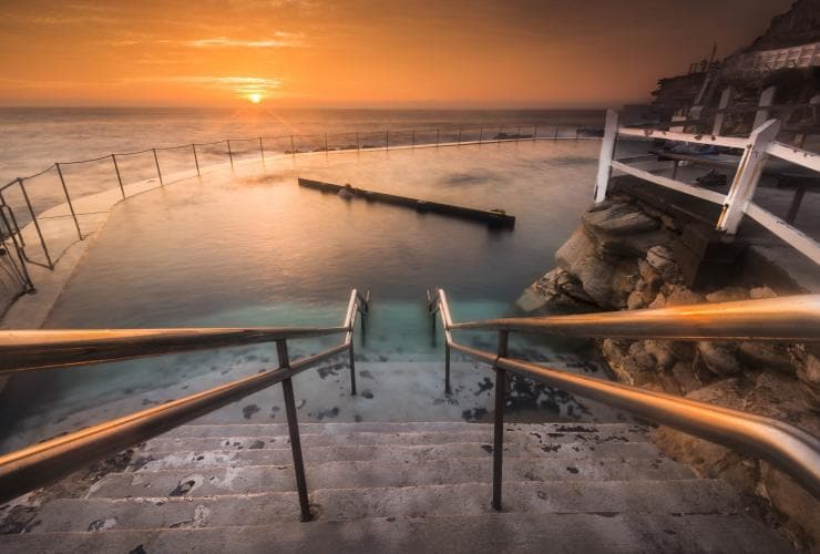 Stairs leading down to the calm, clear water of  Bronte Baths as the sunsets over the ocean, Bronte Beach, Sydney, New South Wales © Destination NSW