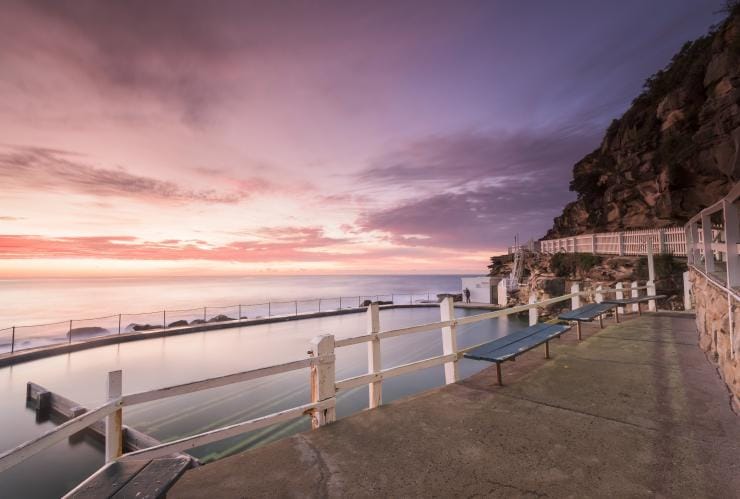 A public seating area above the calm waters of Bronte Baths beneath a purple sky during sunset at Bronte Beach, Sydney, New South Wales © Destination NSW