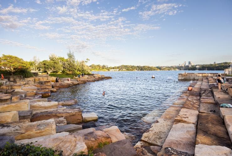 People swimming and lazing on the sandstone rocks surrounding the protected harbour pool of Marrinawi Cove, Barangaroo Reserve, Sydney, New South Wales © Images for Business