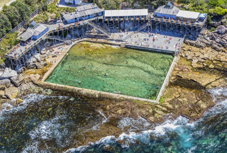 Aerial view over Wylies Baths ocean pool with people swimming and the ocean rolling over coastal rocks surrounding the pool, Coogee, New South Wales © Destination NSW