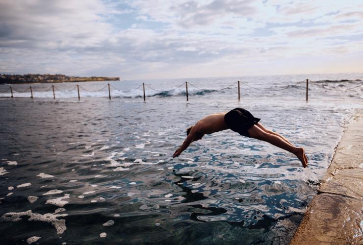 Man diving into the water at Wylies Baths with waves rolling in the ocean behind him in Coogee, New South Wales © Destination NSW