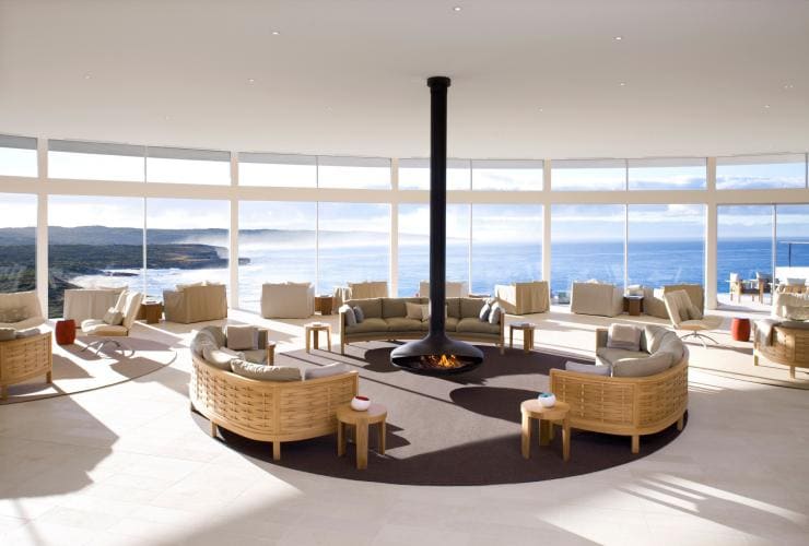 A large, light filled room overlooking the ocean fitted with lounges and chairs surrounding a fireplace at Southern Ocean Lodge, Kangaroo Island, South Australia © Southern Ocean Lodge