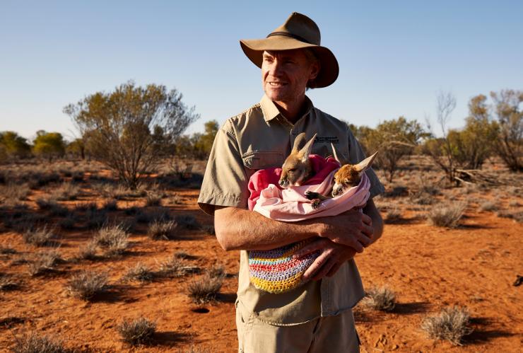 A ranger holding two joeys wrapped up in blankets at the Kangaroo Sanctuary, Alice Springs, Northern Territory © Tourism Australia