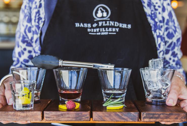 Barman tenant un plateau composé de quatre spiritueux différents, avec des aliments posés devant chaque verre, à la Bass & Flinders Distillery, Mornington Peninsula, Victoria © Bass & Flinders