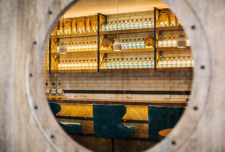 Vue à travers un hublot décoratif sur une gamme de bouteilles d'alcool exposées derrière le bar du Manly Spirits Co., Manly, Nouvelle-Galles du Sud © Alana Dimou