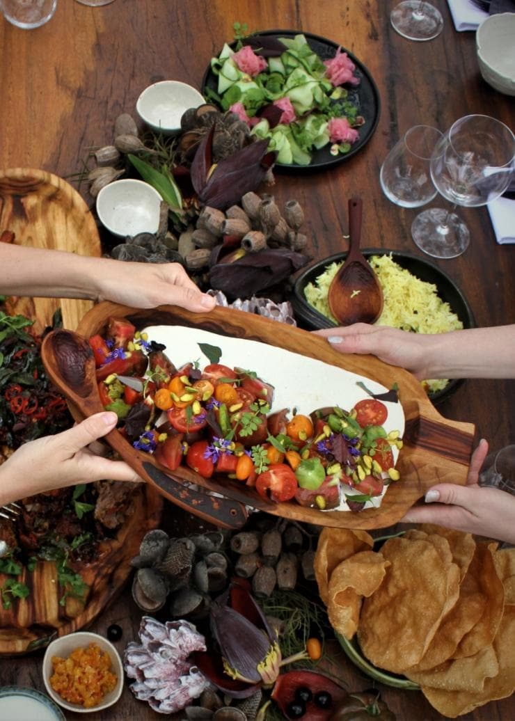 Vue de dessus d'une table remplie de nourriture, par-dessus laquelle deux personnes s'échangent un plat, à Makepeace Island, Noosa, Queensland © Makepeace Island