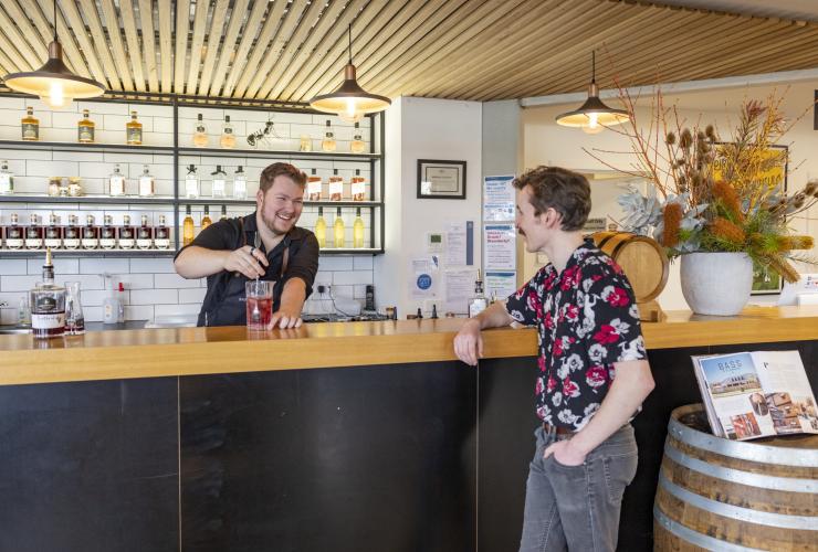 Seorang pria tertawa bersama bartender yang sedang membuat koktail di Bass & Flinders Distillery, Mornington Peninsula, Victoria © Tourism Australia