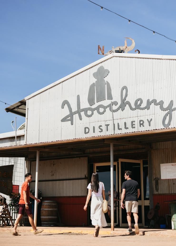 Tiga orang berjalan memasuki gudang timah besar di Hoochery Distillery Café, Kununurra, Western Australia © Tourism Western Australia