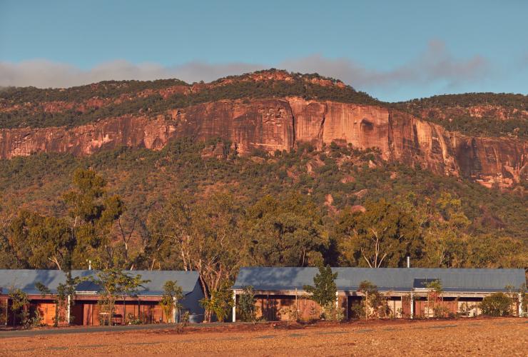Bagian eksterior akomodasi Mt Mulligan Lodge yang terletak di kaki bukit pegunungan berwarna merah yang dipenuhi jajaran pepohonan, Mount Mulligan, Queensland © Jason Ierace