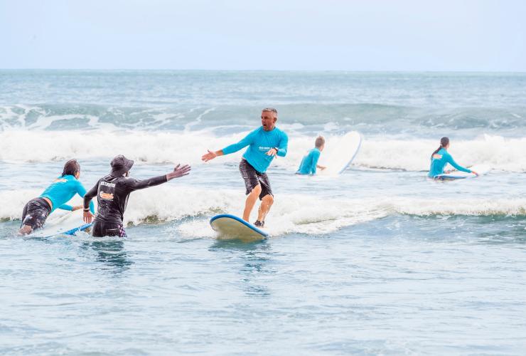 Istruttore immerso nell'oceano fino alla vita che fa un gesto di incoraggiamento con il pugno a un surfista a Noosa, Queensland © Tourism and Events Queensland
