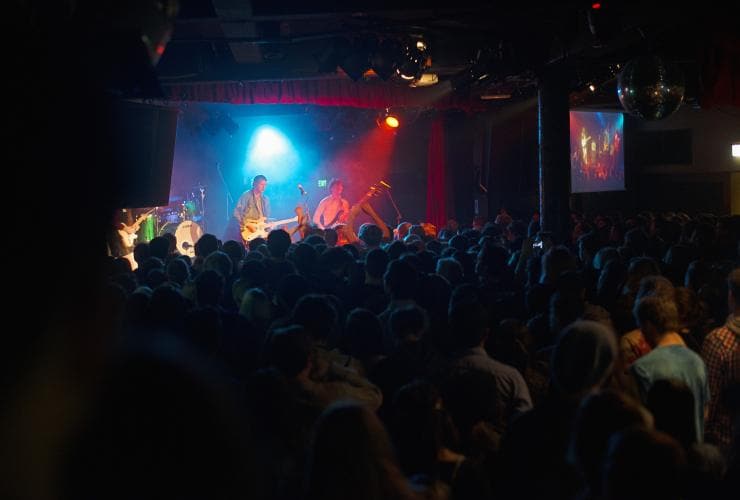 Folla di persone che ballano davanti a una band che suona dal vivo su un palco sotto luci rosse e blu al Corner Hotel, Richmond, Victoria © Visit Victoria