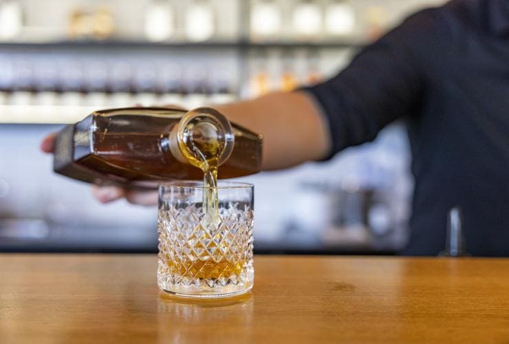 Primo piano di un liquore di colore ambrato che viene versato da una bottiglia in un bicchiere da whisky alla Bass & Flinders Distillery, Mornington Peninsula, Victoria © Tourism Australia