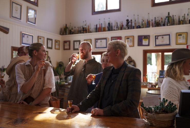 Gruppo di persone che degustano liquori in piccoli bicchieri durante un tour con The Vino Bus alla Tamborine Mountain Distillery, Brisbane, Queensland © Tourism and Events Queensland