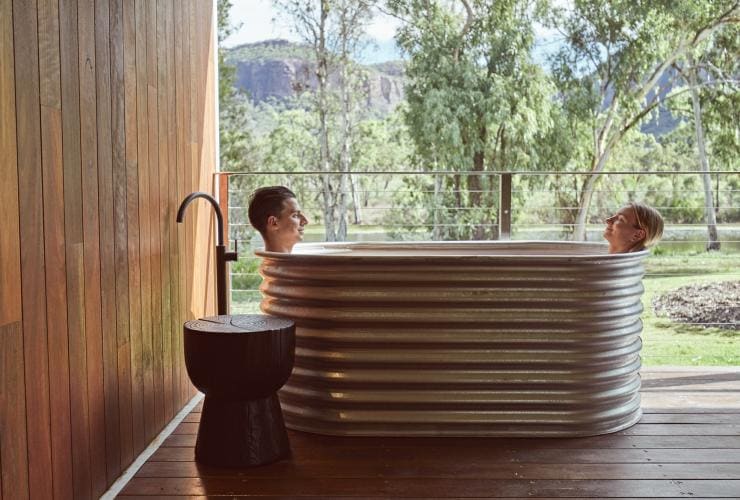 Coppia che fa il bagno sotto il portico della propria accomodation con vista sul paesaggio naturale circostante al Mt Mulligan Lodge, Outback Queensland © Jason Ierace