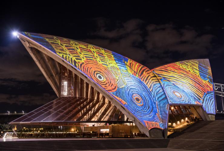 ニュー・サウス・ウェールズ州、シドニー、ブルー・オレンジ・イエローで彩られたオーストラリア先住民のデザインが投影される、船の帆をイメージしたシドニー・オペラ・ハウスの屋根 © Daniel Boud