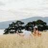 タスマニア州、サテライト島、海を見下ろす丘の草原でピクニックするカップル © Adam Gibson