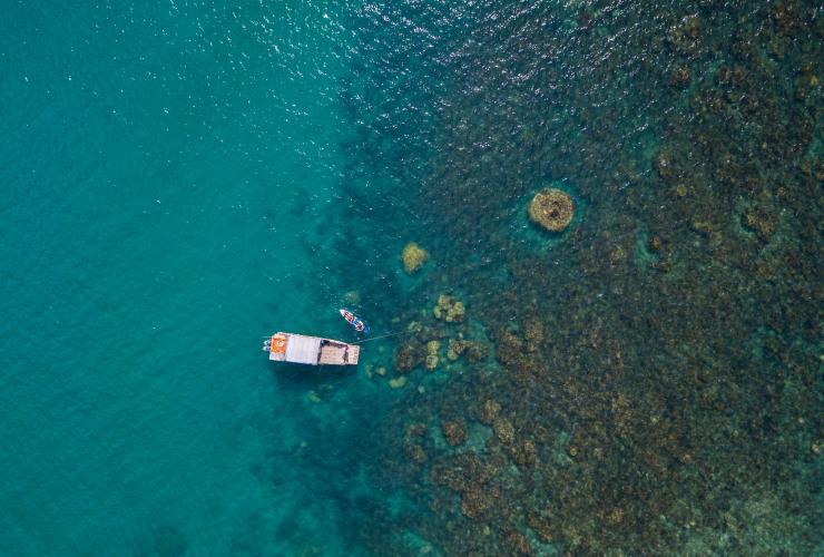 空中俯瞰昆士蘭州聖靈群島露營島小屋附近的珊瑚礁，礁旁有隻小船和有人坐著的獨木舟©露營島小屋